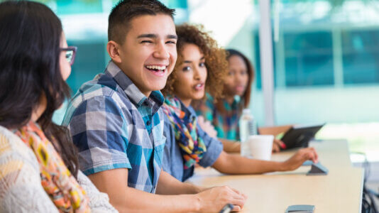 High school newcomer emergent bilingual student laughing with classmates at desk