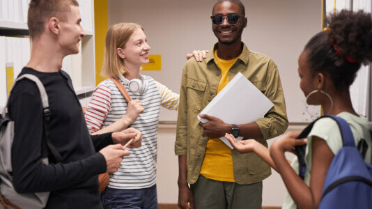 Waist up portrait of diverse group of students chatting with smiling blind man